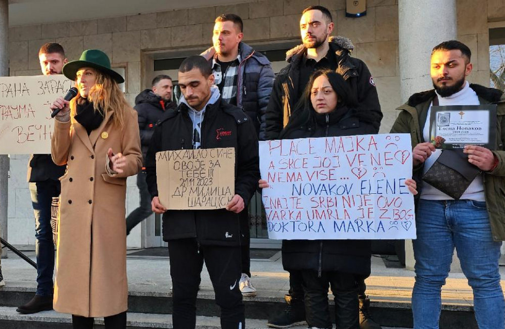 Tüntetés a szülőszobai erőszak ellen, Marica Mihajlović a kép jobb oldalán egy versbe foglalt tiltakozást tartalmazó transzparens tart a kezében, mögött a férje az újszülött Elena Mihajlović gyászjelentésével