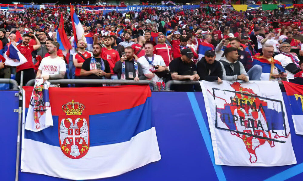 A szerb nacionalizmus szurkolói megnyilvánulása, jobb felől a kifogásolt szerb zászló (transzparens), egy ugyanolyan "lepedő" látható a bal oldalon álló, fehér pólós férfi kezében is