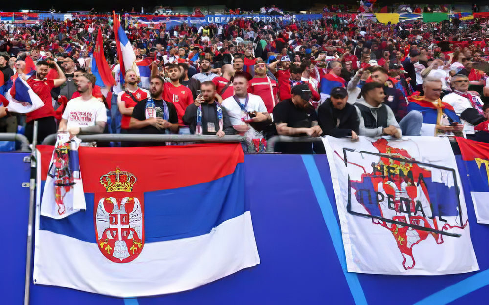 A szerb nacionalizmus szurkolói megnyilvánulása, jobb felől a kifogásolt szerb zászló (transzparens), egy ugyanolyan "lepedő" látható a bal oldalon álló, fehér pólós férfi kezében is
