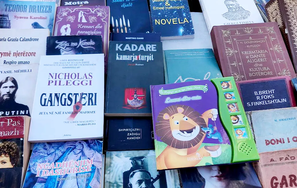 Ismail Kadare az utcai tezgán (albánul asztal, stand): a „Kamarja e turpit” Ismail Kadare 1978-ban megjelent regénye, amelynek magyar címe „A szégyen fülkéje”. A regény központi eleme a „szégyen fülkéje”, egy nyilvános hely, ahol az Oszmán Birodalom a kivégzett lázadók fejét közszemlére teszik, hogy elrettentse a népet