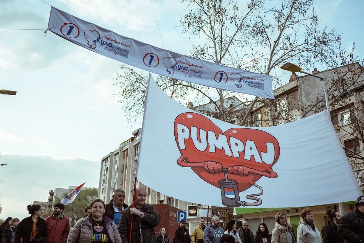Pumpálnak a helyhatósági választások előtt Kúlán a diákokat támogató emberek, fejük felett a kifeszített transzparens hirdeti a szerb elnök listáját